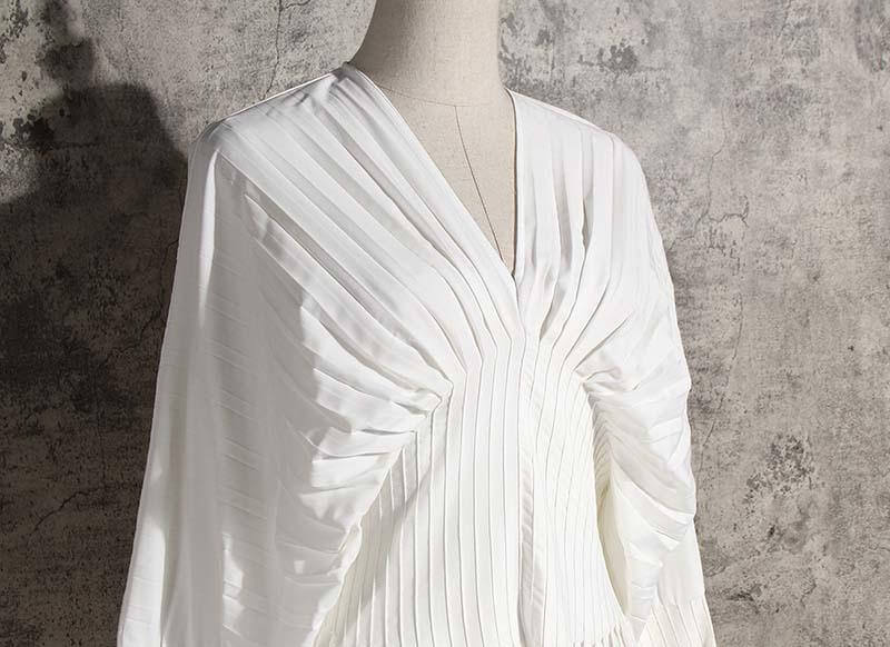 Sakiya pleated long sleeve shirt dress in white on a mannequin against a textured background.