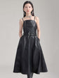 Model wearing a knee-length Musset vegan leather dress in black, featuring spaghetti straps and an A-line silhouette.
